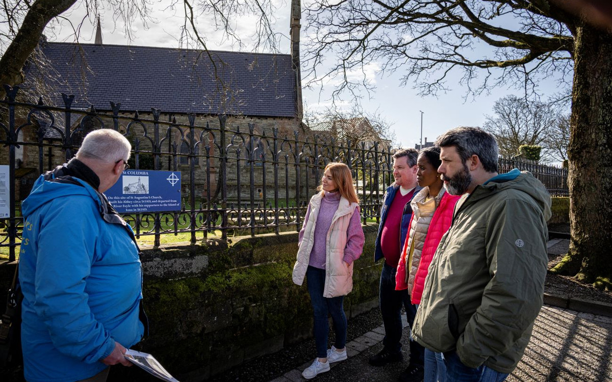 Derry’s ghosts: A darker dander with David Douglas 1 Visitors listening to a guide beside railings and a historic building in Derry.