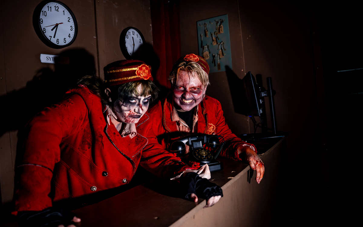The Howl 2026 REVIEW: the most fun I’ve had at a UK scream park 1 Two costumed bellhops in red uniforms at the reception desk inside The Howl's Full Moon Manor.