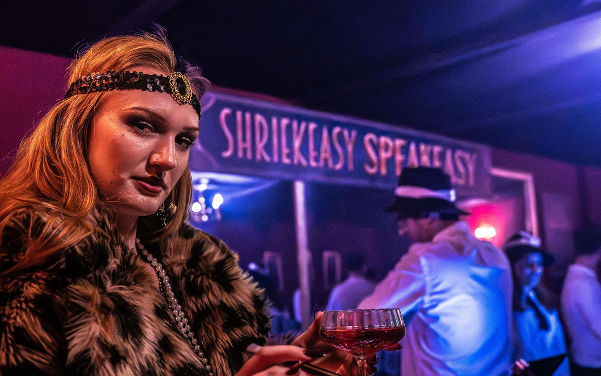 The Howl 2026 REVIEW: the most fun I’ve had at a UK scream park 2 Performer in 1920s-style clothing holding a glass inside The Howl's ShriekEasy speakeasy maze.