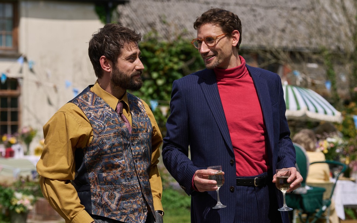BBC confirms The Witch Farm release date 4 Michael Socha as Bill and Edward Holcroft as Max stand together outdoors, with Max holding two wine glasses.