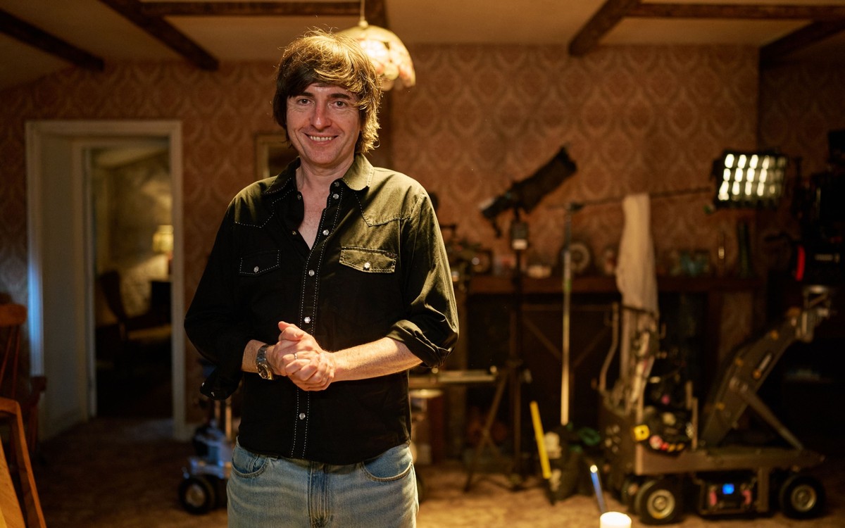 BBC confirms The Witch Farm release date 1 Danny Robins stands on The Witch Farm set with lighting and camera equipment behind him.